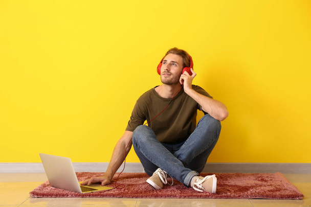 Young man with laptop listening to music near color wall - Φωτογραφία, εικόνα