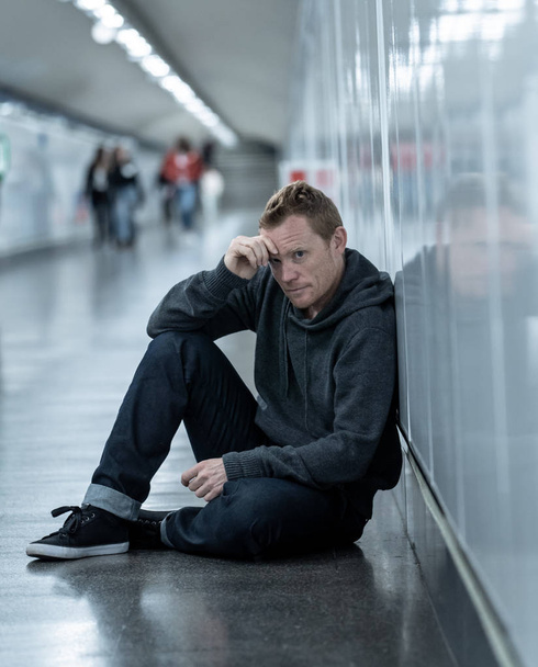 Miserable jobless young man crying Drug addict Homeless in depression stress sitting on ground street subway tunnel looking desperate leaning on wall alone in Mental disorder Emotional pain Sadness. - Фото, изображение