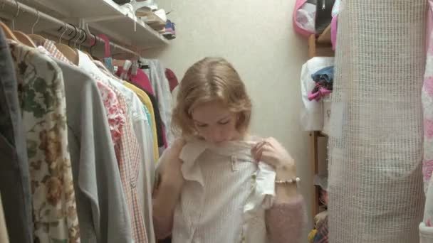 Mooi meisje glimlacht en hangers met kleren doorloopt in haar kleedkamer - Video
