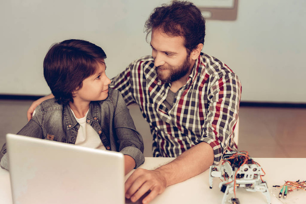 Bearded Father Help Son to Program Robot at Home. Young Boy in Shirt. Using Laptop. Modern Hobby Concept. Modern Technology. Robot Engineering Concept. Bearded Young Man. Innovation for Fun. - Foto, imagen