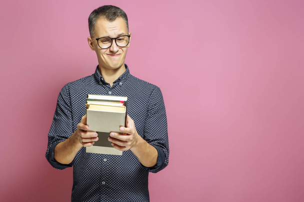 Surprised man with a stack of books on a pink background. - Foto, imagen