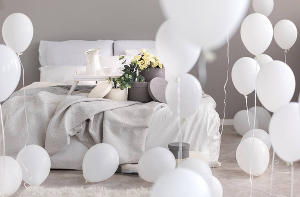 Balloons in industrial stylish bedroom with grey bedding, trey with coffee cups and round boxes with flowers on th bed - Valokuva, kuva