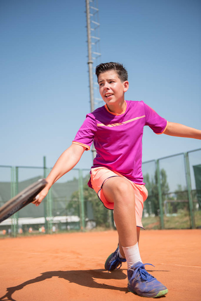 Young tennis player playing backhand and glide - Фото, изображение