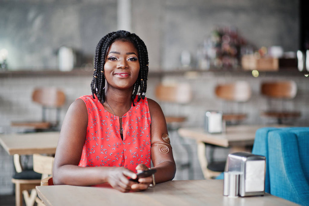 attraktive Afroamerikanerin sitzt mit Handy an der Hand am Tisch eines Cafés. - Foto, Bild