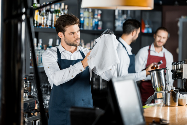 adult barman in apron rubbing up wine glass with cloth - Фото, зображення