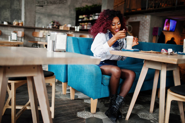 attraktive afrikanisch-amerikanische lockige Mädchen sitzt im Café mit Latte. - Foto, Bild