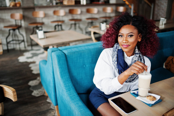 Привлекательная африканская кудрявая американка сидит в кафе с латте
. - Фото, изображение