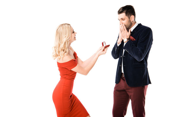 Attractive woman proposing surprised boyfriend with ring isolated on white - Photo, Image