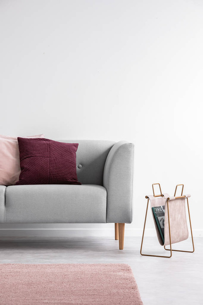 Purple and pastel pink pillow on the grey couch in bright living room interior, real photo with copy space on the empty white wall - Foto, Bild