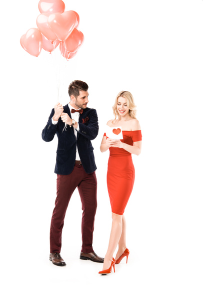 Knappe man met rode ballons terwijl vrouw leest briefkaart geïsoleerd op wit - Foto, afbeelding