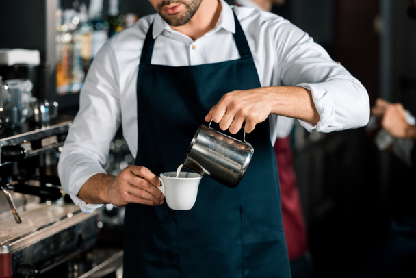 обрізаний вид на бариста в фартусі, що заливає молоко до кави на робочому місці
 - Фото, зображення