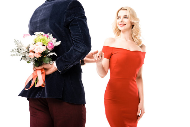 Rückansicht eines Mannes mit Blumen hinter dem Rücken, der die Hand seiner Freundin hält, isoliert auf weiß - Foto, Bild