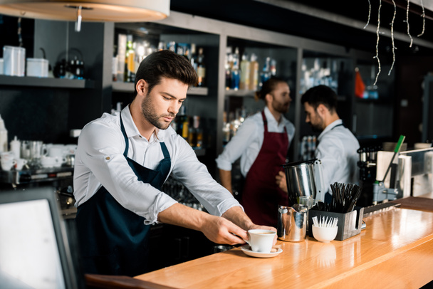 bonito barista no avental colocando xícara de café no balcão de madeira
 - Foto, Imagem