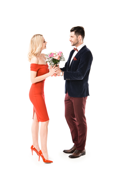Seitenansicht eines Mannes im Anzug, der seiner schönen Freundin Blumen schenkt, isoliert auf Weiß - Foto, Bild