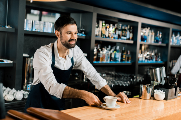веселый улыбающийся бариста, подающий кофе у деревянного прилавка
 - Фото, изображение