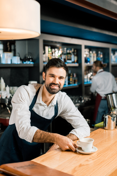 cheerful smiling barista with coffee at wooden table  - Photo, Image