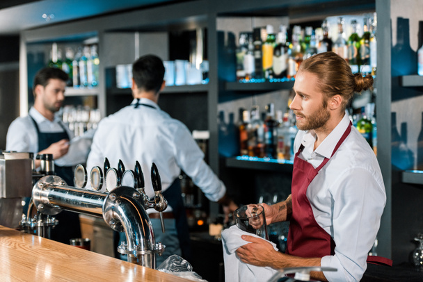 thoughtful barman polishing glass with cloth at wooden counter - Photo, Image