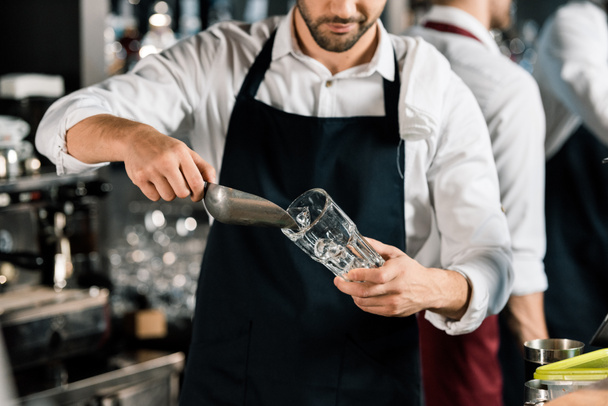 cropped view of  barman in apron putting ice in glass with ice shovel - Foto, Imagem