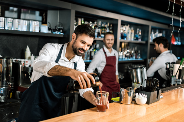 smiling bartender pouring cocktail in glass at wooden counter - Photo, Image