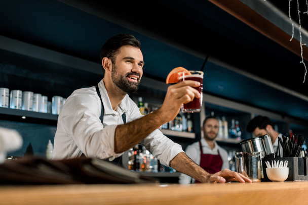 smiling bartender serving cocktail at wooden counter - Foto, imagen