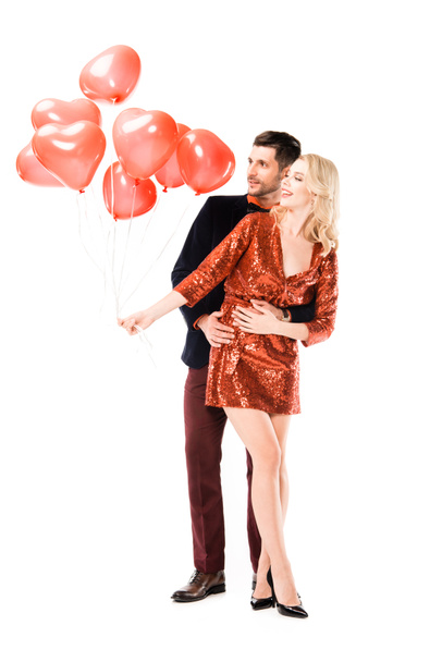schönes romantisches Paar, das sich umarmt, während es rote Luftballons auf weißem Grund hält - Foto, Bild