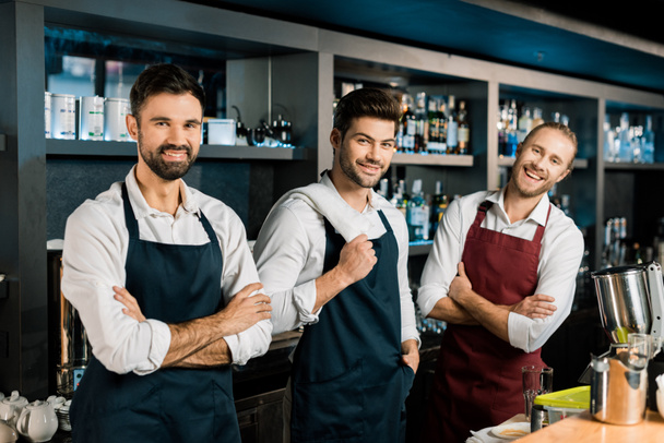 equipo de barmen adulto en delantales de pie en el lugar de trabajo con los brazos cruzados
 - Foto, Imagen