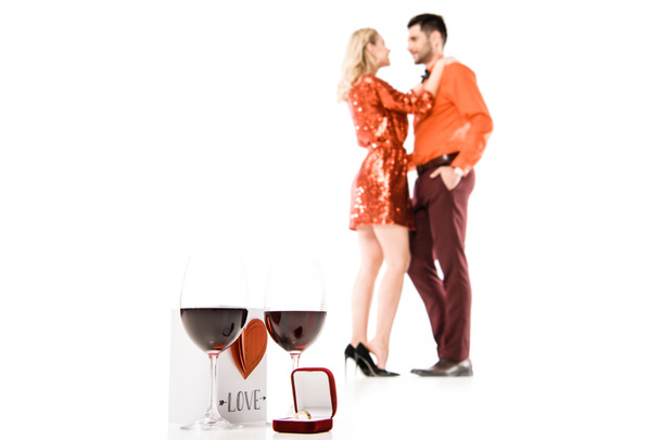 Δύο ποτήρια κρασί, όμορφη καρτ ποστάλ και κουτί δαχτυλίδι στο φόντο της αγκάλιασμα ζευγάρι που απομονώνονται σε λευκό - Φωτογραφία, εικόνα