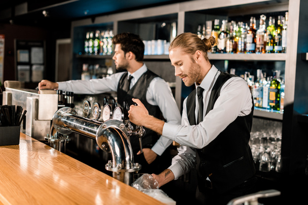 Handsome barman standing and working with coworker in bar - Foto, Imagem