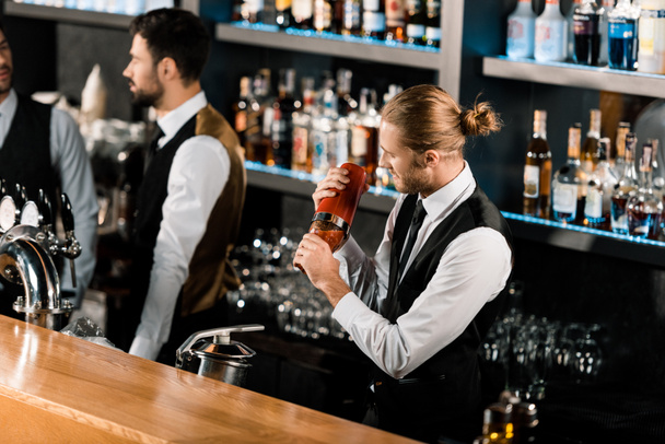Barman mezcla cóctel en la coctelera y de pie en el bar
 - Foto, imagen