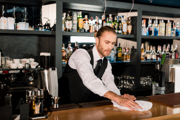 Bartender cleaning wooden bar counter with white napkin - Fotó, kép