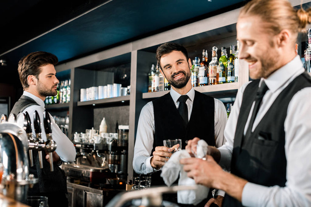 Camareros guapos sonriendo en el bar y limpiando vasos
  - Foto, Imagen