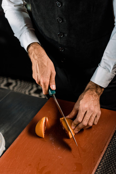 Чоловічі руки розрізають фрукти на обробній дошці ножем
 - Фото, зображення