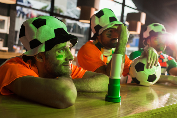 Football fans sitting in hats, watching soccer in bar - 写真・画像
