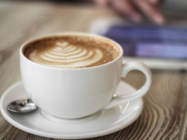 cup of coffee on a wooden table on a background of young woman works with digital tablet - Photo, Image