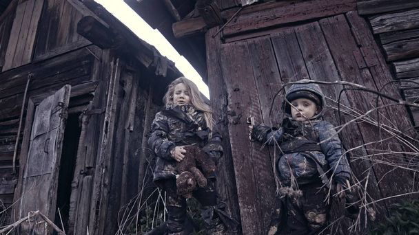 portrait of little dirty homeless kids with bear toy crying against abandoned building - Фото, зображення