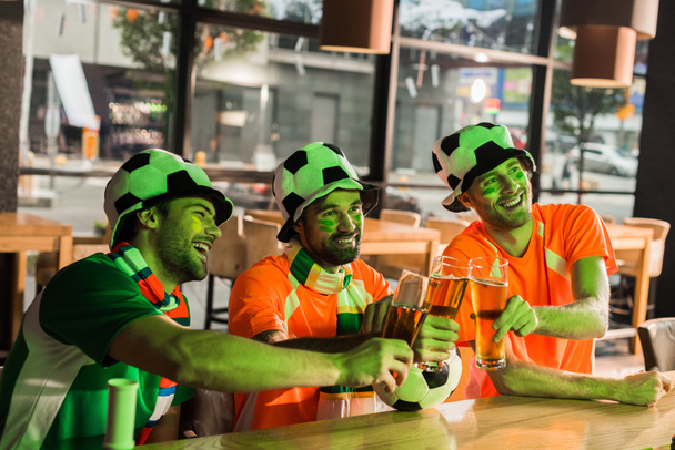 Football fans watching soccer and holding glasses with lager in bar - Photo, Image