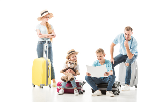 Happy family sitting on baggage and looking on map isolated on white - Fotó, kép
