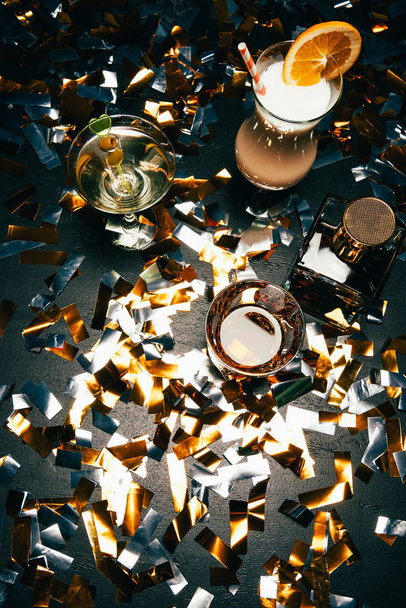 view from above of whiskey, alcoholic cocktails with orange slice and olives on table covered by golden confetti  - Φωτογραφία, εικόνα