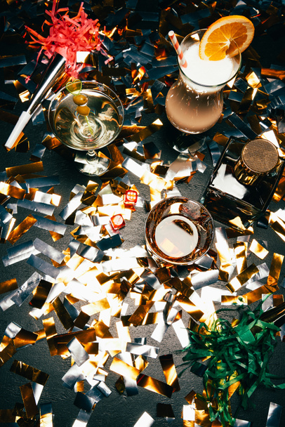 view from above of alcoholic cocktails, whiskey and party horns on table covered by golden confetti  - Photo, Image
