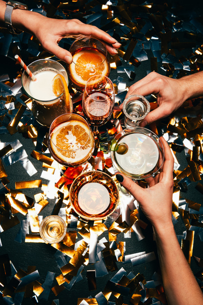 partial view of friends clinking by cocktail glasses at table covered by golden confetti  - Foto, Imagem