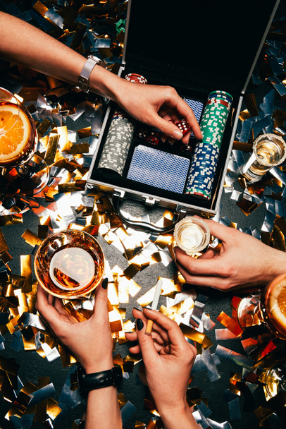 vista parcial de amigos celebrando con alcohol, cigarrillos y naipes en la mesa cubierta por confeti dorado
  - Foto, Imagen