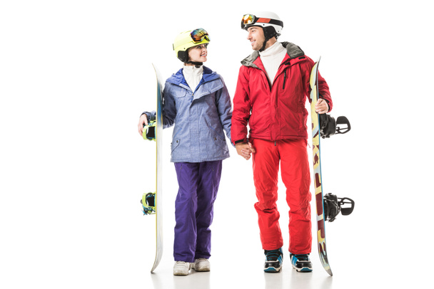 pareja sonriente en trajes de esquí sosteniendo tablas de snowboard y mirándose aislados en blanco
 - Foto, imagen