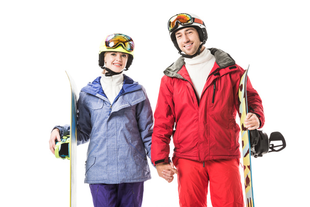 Pareja en trajes de esquí con tablas de snowboard cogidas de la mano, sonriendo y mirando a la cámara aislada en blanco
 - Foto, imagen