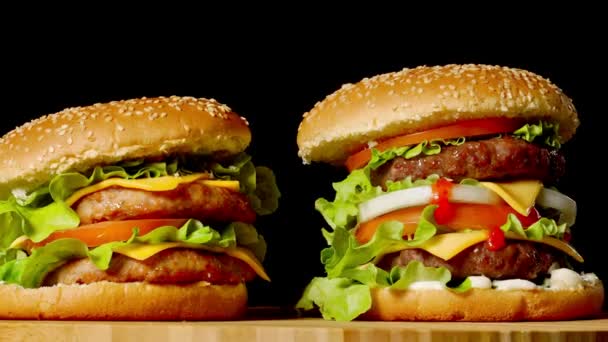 Η έννοια της American fast food. Ζουμερά αμερικανική μπιφτέκι με δύο μοσχάρι κοτολέτες, σάλτσα και ogretsami σε μαύρο φόντο. Χώρο αντίγραφο - Πλάνα, βίντεο