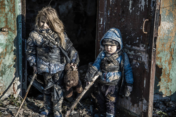 portrait of little dirty homeless kids with bear toy beside abandoned building - Fotó, kép