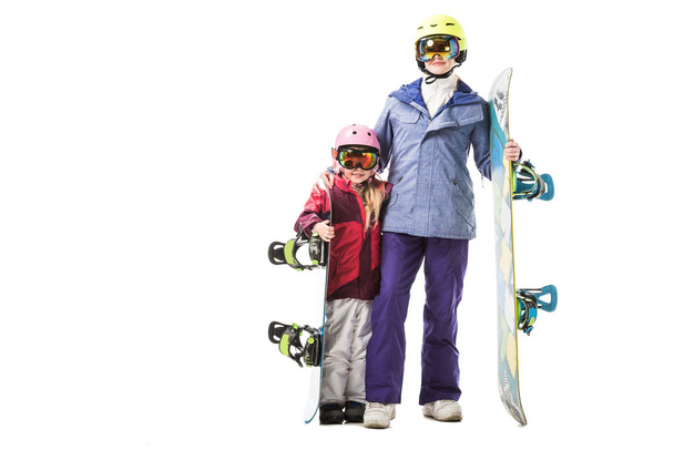 äiti ja esikoululainen tytär hiihtopuvuissa, suojalaseissa ja kypärissä, joiden lumilaudat hymyilevät eristyksissä valkoisella
 - Valokuva, kuva