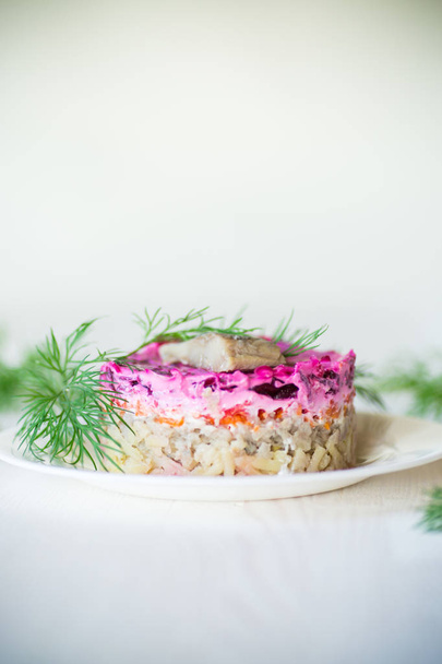 layered salad of boiled vegetables with beets and herring on a plate with greens - Foto, immagini