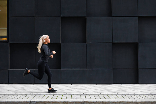 Woman running on the city street against modern city walls - Foto, imagen