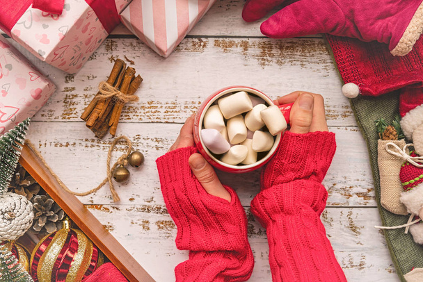 Kerstmis en Nieuwjaar concept.female handen met Mok met marshmallows en geschenken, lag kous en decorationstop weergave plat op witte houten achtergrond - Foto, afbeelding