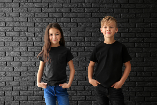 Schattige kinderen in t-shirts tegen donkere bakstenen muur - Foto, afbeelding
